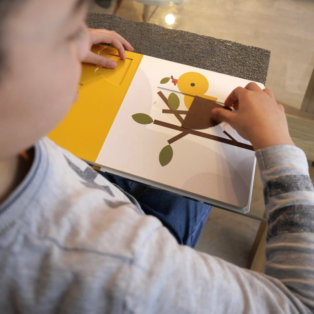 Un enfant interagit avec plaisir avec un livre pop-up réalisé par un studio de création, mettant en scène un oiseau perché sur une branche. Limbus Studio