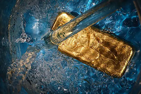Un lingot d'or immergé dans de l'eau bleu clair avec des bulles et un jet de liquide en cascade dessus, incarnant l'essence du design élégant. Limbus Studio