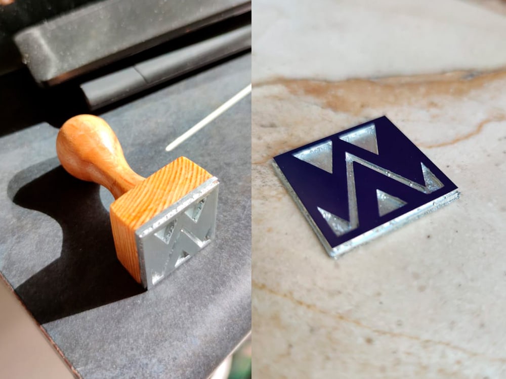 Un tampon à manche en bois avec un logo « W », réalisé avec art grâce à un design créatif, se trouve à côté d'un carré bleu marine estampé comportant un « W » argenté sur la table. Limbus Studio