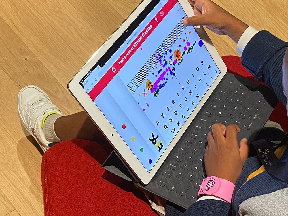 Un enfant utilisant une application de clavier colorée sur une tablette, assis confortablement sur un coussin rouge sur le plancher en bois, met en valeur sa créativité, un peu comme s'il construisait un site Web unique sur WordPress. Limbus Studio