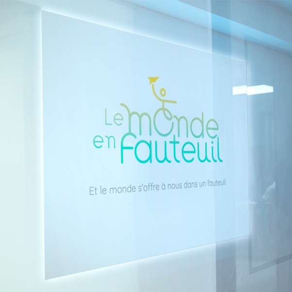 Un panneau lumineux indique "Le monde en fauteuil" avec un graphique en fauteuil roulant, un texte en français en dessous et le hashtag #lemondeenfauteuil - votre destination pour découvrir le fauteuil en ligne. Limbus Studio
