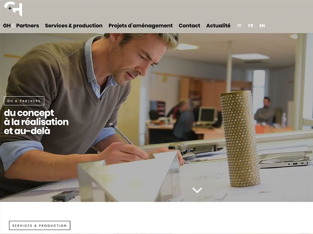 Un homme travaille méticuleusement à son bureau, entouré de modèles et de dessins architecturaux, incarnant une approche axée sur le design dans le cadre de son bureau d'agence. Limbus Studio