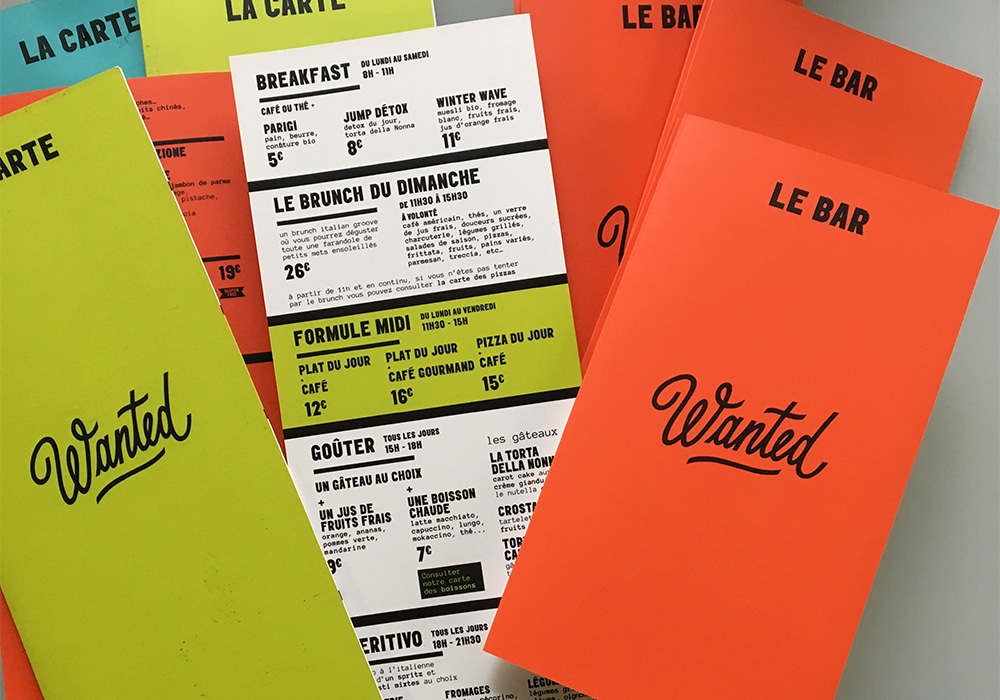 Des menus de restaurant colorés, conçus et intitulés « Wanted » en vert, jaune et orange, proposant des options de petit-déjeuner et de brunch. Une véritable création culinaire qui captive à la fois l'œil et le palais. Limbus Studio