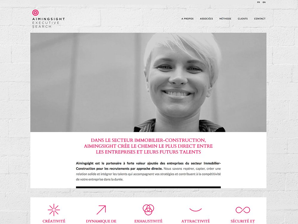 Une personne souriante aux cheveux courts est présentée sur le site Web d'Aiminsight Executive Search, mêlant harmonieusement des informations sur l'immobilier et les talents à des éléments de conception élégants. Limbus Studio