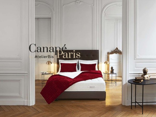 Chambre studio élégante avec murs blancs, parquet et literie rouge mettant en valeur un design raffiné. L'éclairage décoratif ajoute une touche de sophistication. Texte : "Canapé Paris AtelierBis via WordPress. Limbus Studio