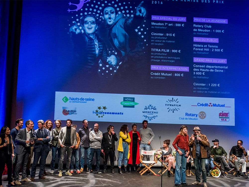 Un groupe de personnes se tient sur une scène avec un grand écran affichant des récompenses et des logos en arrière-plan, célébrant l'excellence en matière de conception et d'innovation au sein de la communauté WordPress. Limbus Studio