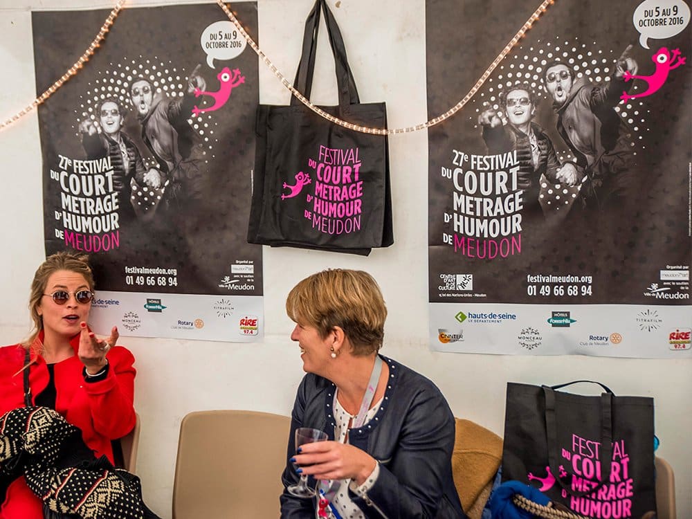 Deux femmes sont assises sur un banc, discutant avec animation devant des affiches du Festival du court-métrage de Meudon, leur conversation dérivant parfois vers les dernières tendances en matière de conception WordPress. Limbus Studio