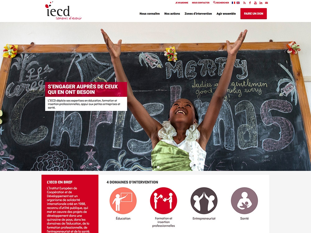 Une fille lève joyeusement les bras devant un tableau noir orné de décorations de Noël et du logo de l'iedc, capturant l'essence de la créativité festive que toute agence de graphisme admirerait. Limbus Studio