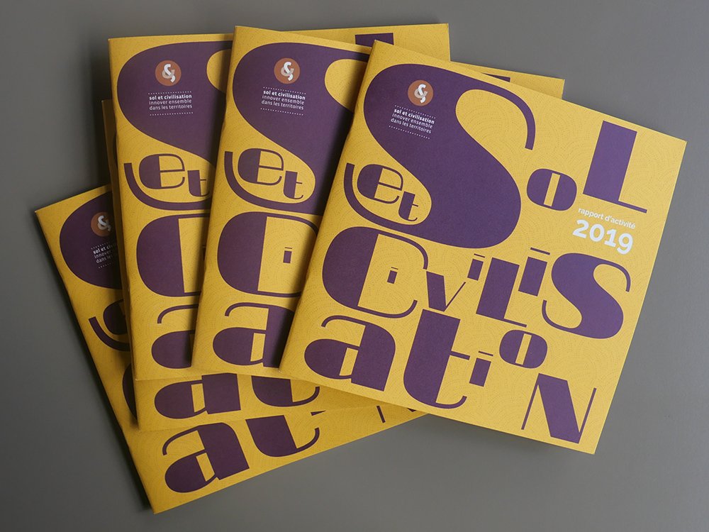 Pile de rapports annuels 2019 jaunes et violets avec un design de texte abstrait sur la couverture, mettant en valeur les prouesses créatives de l'art axé sur l'agence. Limbus Studio