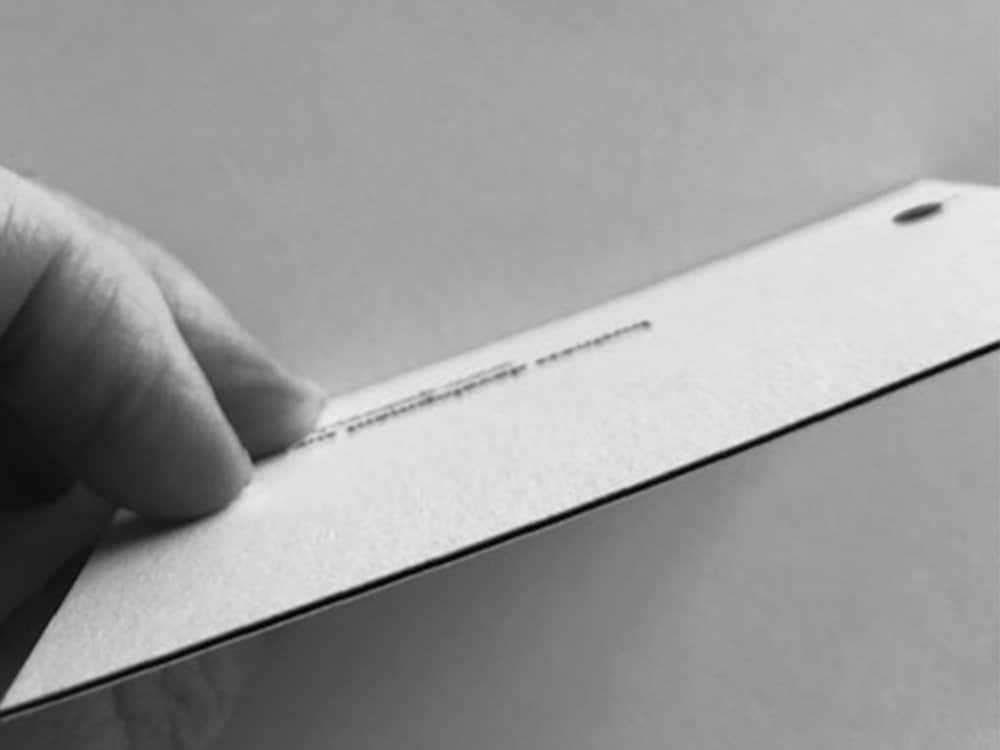 Gros plan d'une main tenant une carte vierge et texturée avec un trou dans le coin, rappelant une invitation réalisée par une agence de création, sur un fond uni. Limbus Studio